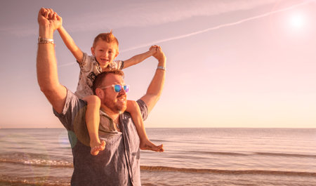 dad with son on his shoulders looking at the horizon in the water at the seaの写真素材