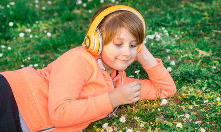 girl lying on the grass listens to music and picks up daisiesの写真素材