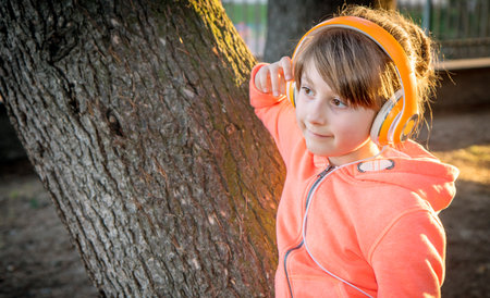 young girl is listen music with headphone to the park