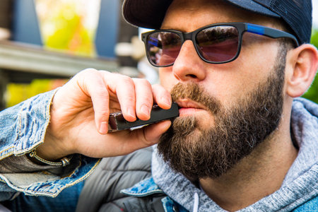 man with a beard smokes an electronic cigarette