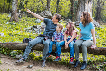 Happy family are sitting on the trunk of a tree in a forestの写真素材