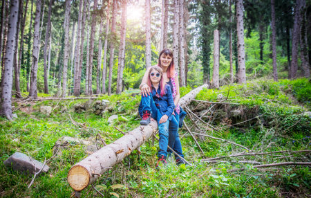 mother and daughter are sitting on trunk of tree in the forest