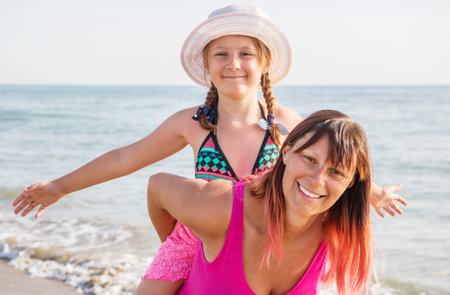 Portrait of smiling happy mother and little daughter laughing together on sunny beachの写真素材
