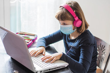 Pretty schoolgirl studying homework math during her online lesson at home, social distance during quarantine, self-isolation, online education concept, home schoolerの写真素材