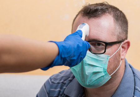 Coronavirus nurse wearing gloves and holding medical infrared forehead thermometer to check body...