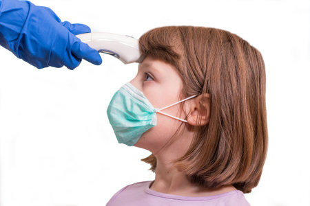 Pediatrician or doctor checks elementary age girl's body temperature using infrared forehead...