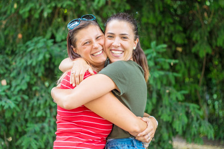 Portrait of two young beautiful lesbian smiling girls hug each other in a summer day whit colored t-shirt clothes and jeansの写真素材