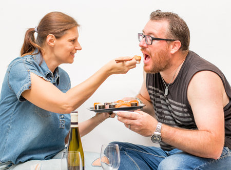 Portrait of attractive  couple  eating japanese food together on the sofa. Couple relaxing on home...