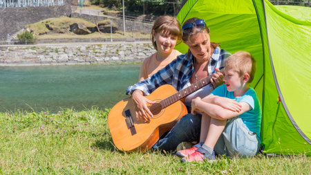 A happy family camping at the river, playing the guitar and singing a song together in the tent.の写真素材
