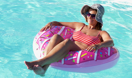 smiling woman is resting on the donut inflatable on the swimming poolの写真素材