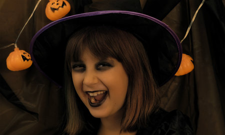 young little girl dressed as a witch surrounded by bright pumpkins celebrates halloweenの写真素材