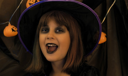 young little girl dressed as a witch surrounded by bright pumpkins celebrates halloweenの写真素材