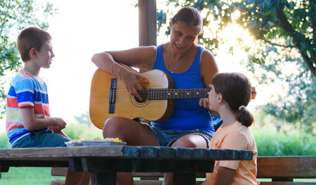 Mom and her two children sing songs together playing guitar outdoors on a sunny day. Concept of relaxation and healthy lifeの写真素材