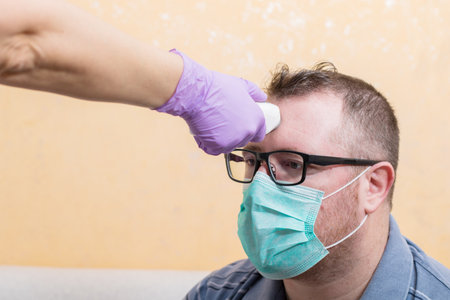 Coronavirus nurse wearing gloves and holding medical infrared forehead thermometer to check body temperature for virus symptoms. Initial screening to prevent the coronavirus outbreak. Healthcare concept.の写真素材