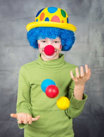 young child dressed as a clown with wig and fake nose has fun playing with colorful balls celebrating carnivalの写真素材