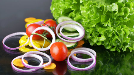 fresh salad with tomatoes, onion ring, cucumber and yellow pepper on black glass backgroundの写真素材