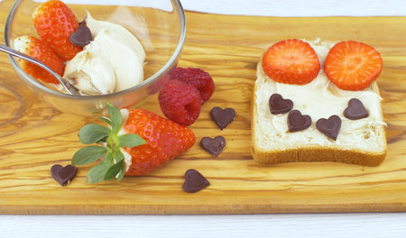 Healthy funny food art breakfast toast for kids. Making a smiling face toast with chocolate nut butter, strawberry and chocolate heartの写真素材