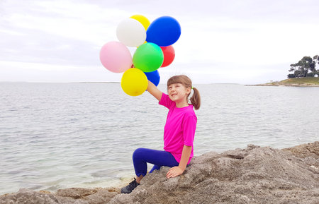 Little girl playing with colored balloons on the rock at the seaの写真素材