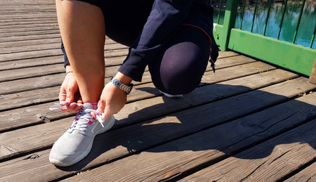 Young athlete woman tying running shoes in the park outdoor