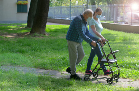 Young caregiver accompanies an elderly gentleman helping him to walk in the parkの写真素材