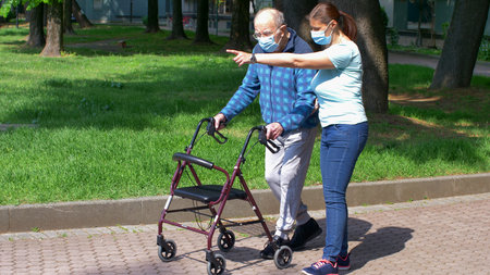 Young caregiver accompanies an elderly gentleman helping him to walk in the parkの写真素材