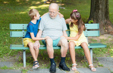 happy children and theri grandfather are playing time together on the bench in the parkの写真素材