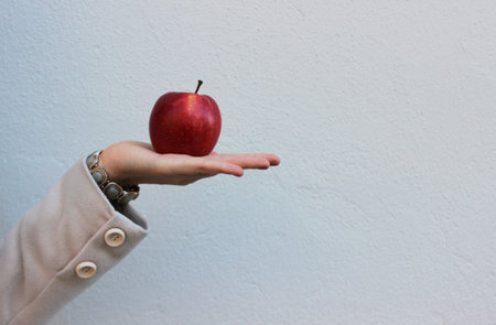 woman in a coat holds a red tasty appleの写真素材