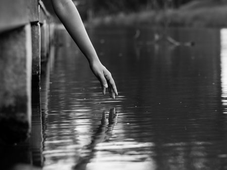 A hand reaching to water surface with reflectionの写真素材