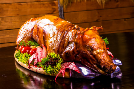 Roasted piglet decorated with vegetables and ham on platterの写真素材