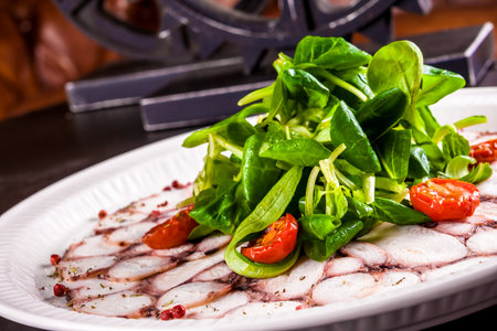 Carpaccio of octopus with corn salad on white plateの写真素材