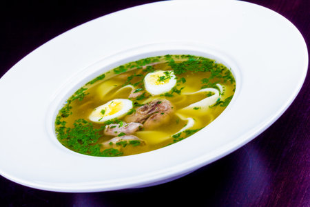 Soup with meat, quail eggs and noodles in white plateの写真素材