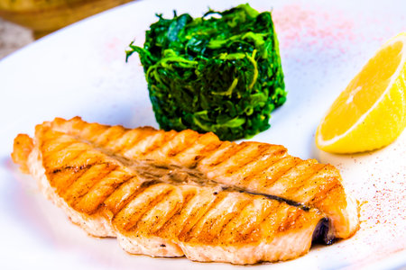 Grilled salmon steak with stewed spinach on white plateの写真素材