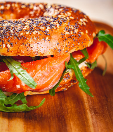 Bagel with cream cheese, smoked salmon and arugula salad on wooden board. Close up