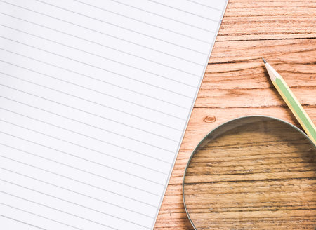 Closeup shot of blank paper with pencil and magnifier on teak wood board.の写真素材