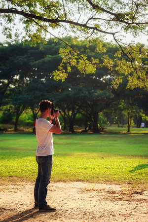 Young man is taking a photo in a park during sunset.の写真素材