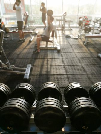 Rows of dumbbells and unidentified people are working out in the fitness gym.の写真素材