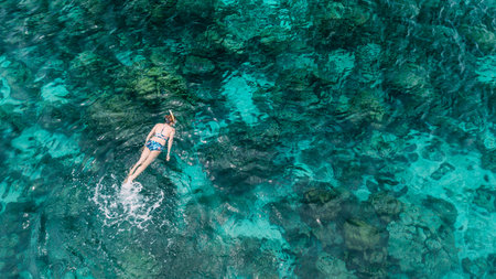 Woman swimming in blue sea. Snorkeling girl in full-face snorkeling mask. Coral reef in shallow sea. Snorkel undersea. Seashore underwater photo. Active seaside vacation. Water sport in tropical sea.の写真素材