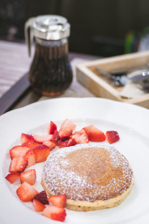 Close-up delicious pancakes, with fresh blueberries, strawberries and maple syrup on a light background. With copy space. Sweet maple, Apple syrup syrup flows from a stack of pancake.の写真素材