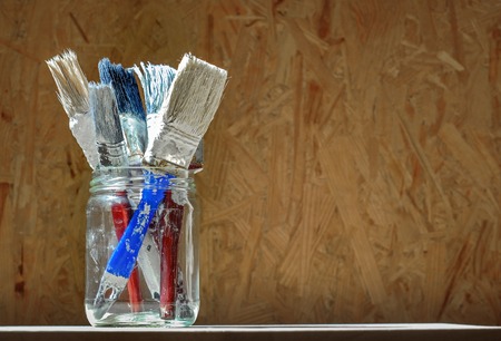 Old paint brushes in a glass jar on wooden panel backgroundの写真素材