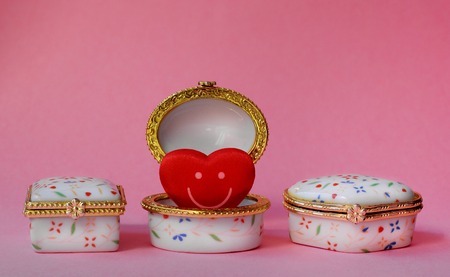 Jewelry boxes with one having a red smiley heart inside on pink backgroundの写真素材