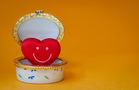 Jewelry box with a red smiley heart inside on yellow backgroundの写真素材
