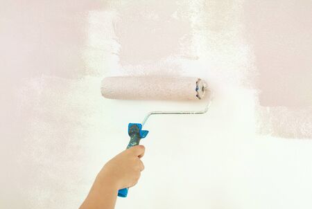 Woman with roller painting wall with pink color