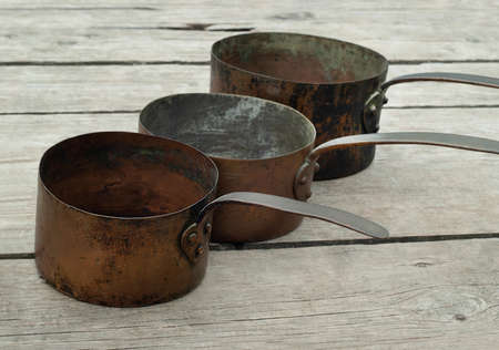 Antique rusty copper pots on wooden background