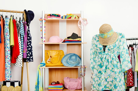 Wardrobe with summer clothes nicely arranged and a beach outfit on a mannequin Dressing closet with colorful clothes and accessories on hangers and a shelf の写真素材