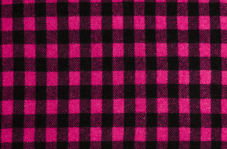 Closeup on checkered tablecloth wool fabric. Magenta pink with black gingham square pattern as...