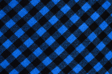 Closeup on checkered tablecloth wool fabric. Blue with black gingham square pattern as background.