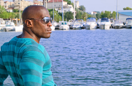 Summer marine scene with a handsome black man. Attractive man wearing a blouse with stripes at the sea side. Yachts in the background.の写真素材