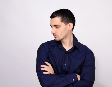 Man standing with his arms crossed looking down over the shoulder to the side from profile. Portrait of a young business man wearing a dark blue shirt.の写真素材