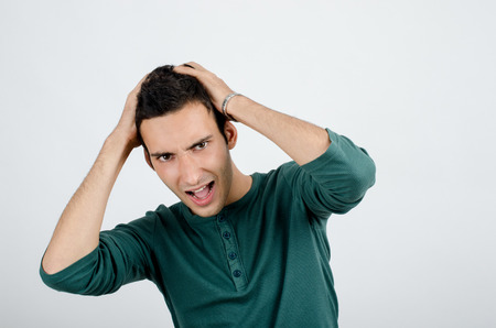 Young man holding his head frowning with worry screaming. Man pulling his hear for worry, sadness,...