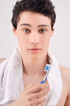 Morning routine of washing the teeth. Handsome young man with towel around the neck holding a toothbrush.の写真素材